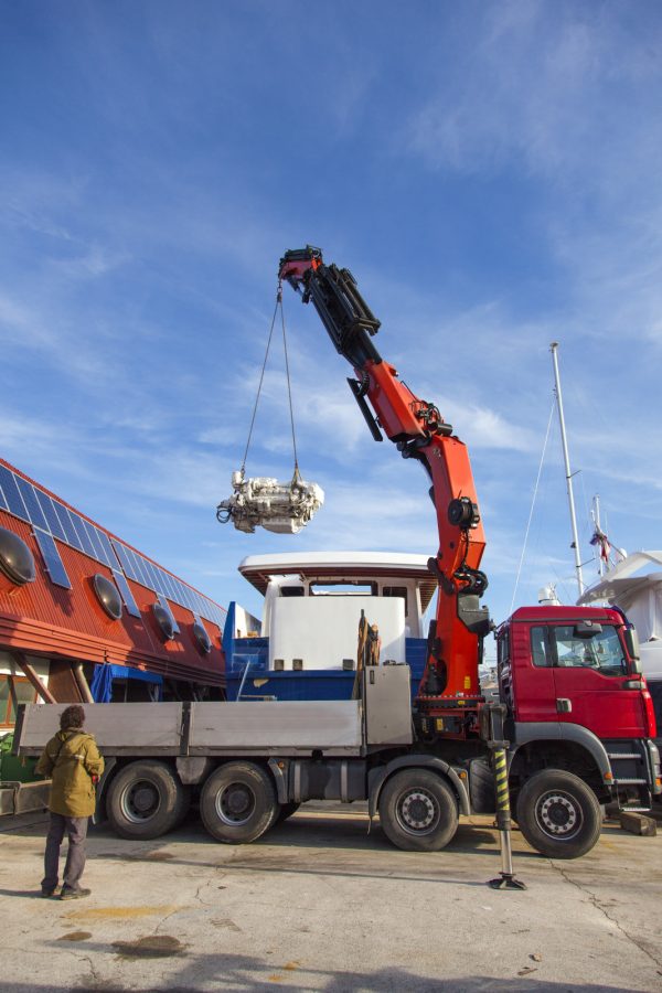 Truck with a telescopic crane lifting a yacht engine